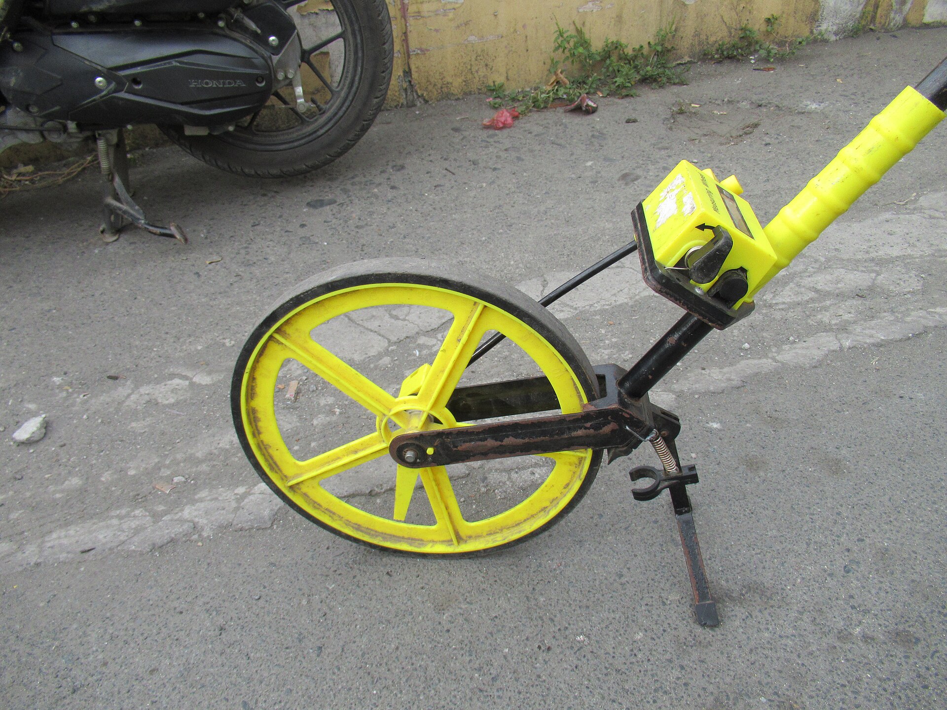 Yellow surveyor measuring wheel standing on pavement