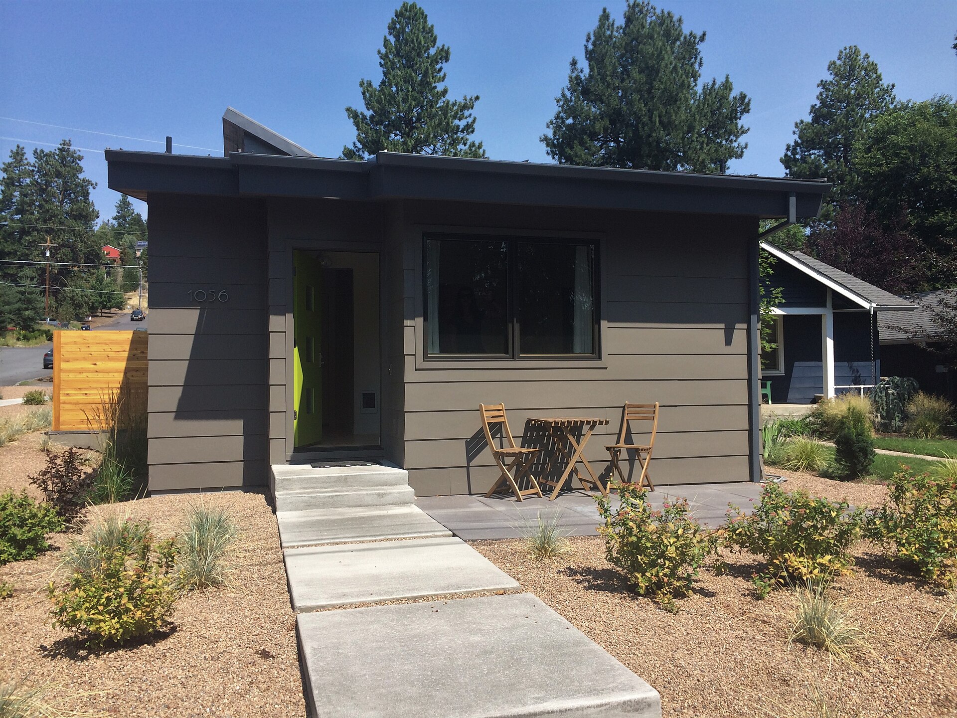 Small modern detached backyard cottage with dark siding, a concrete path and young landscaping