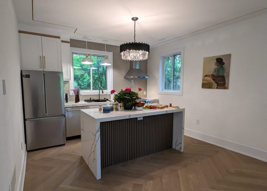 Bright open kitchen inside a new backyard garden suite with white cabinets, island and pendant light