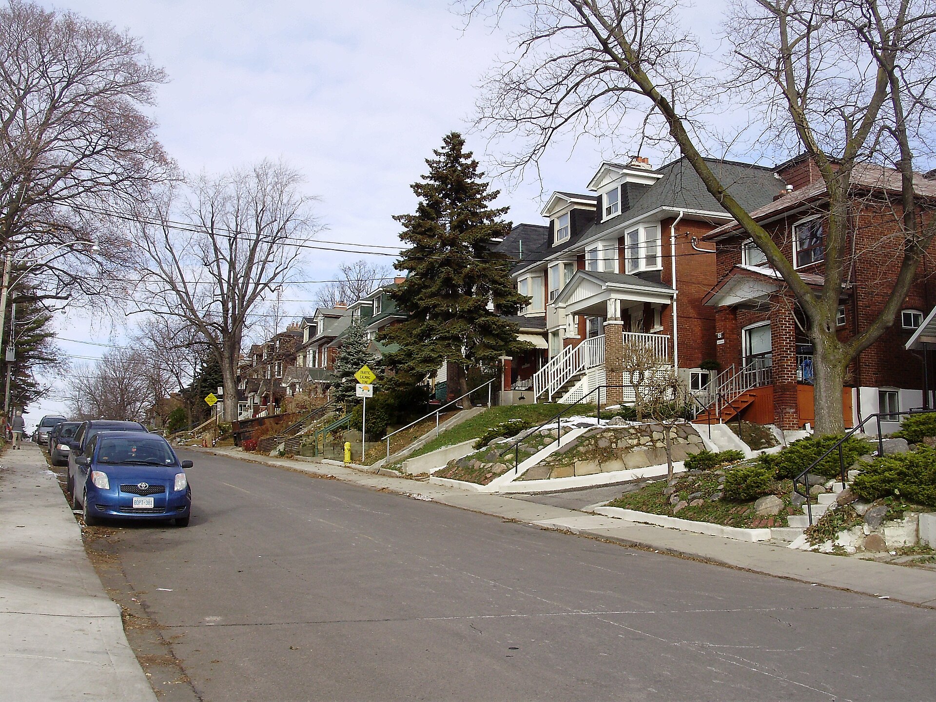 Row of older brick houses with porches and mature trees along Alberta Avenue in Toronto’s Wychwood neighbourhood