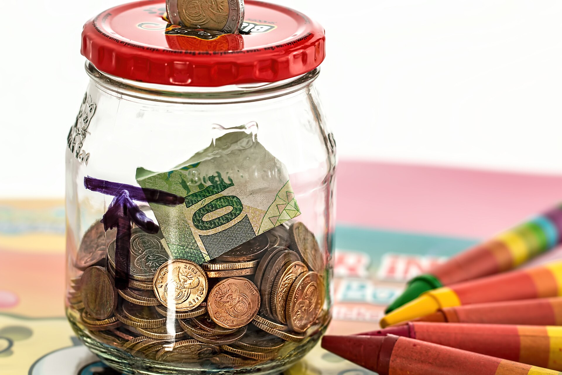 Glass jar filled with coins and folded banknotes used as a savings jar