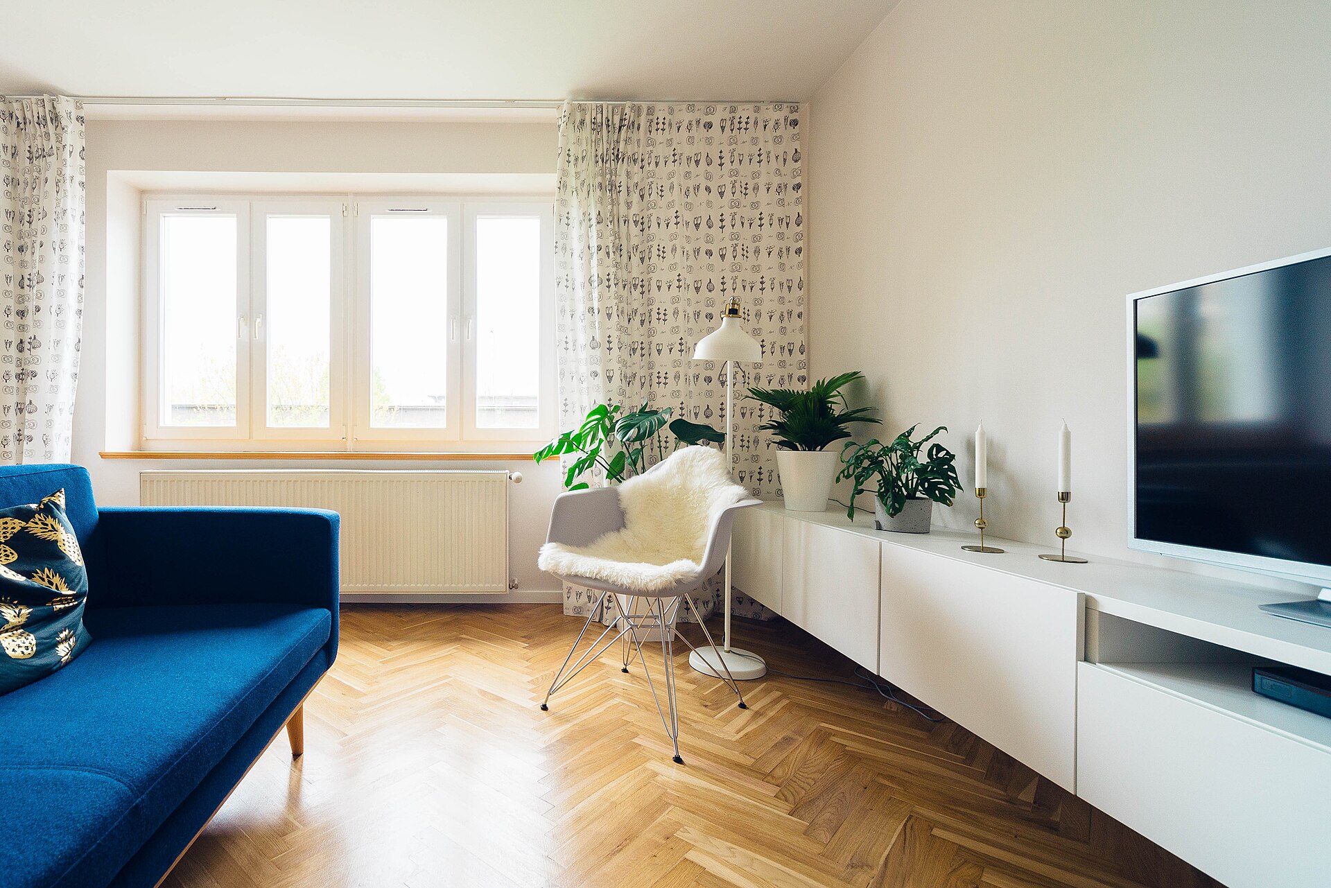 Bright, tidy living room with a blue sofa, white media cabinet and tall windows