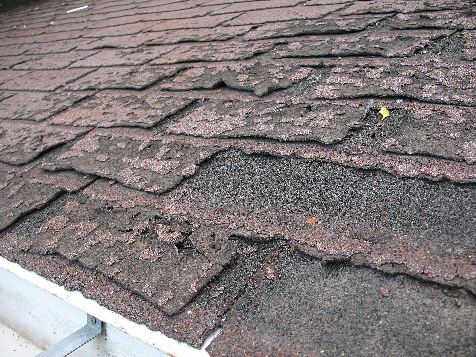 Close-up of old asphalt roof shingles that have shrunk, cracked and lost their granule coating