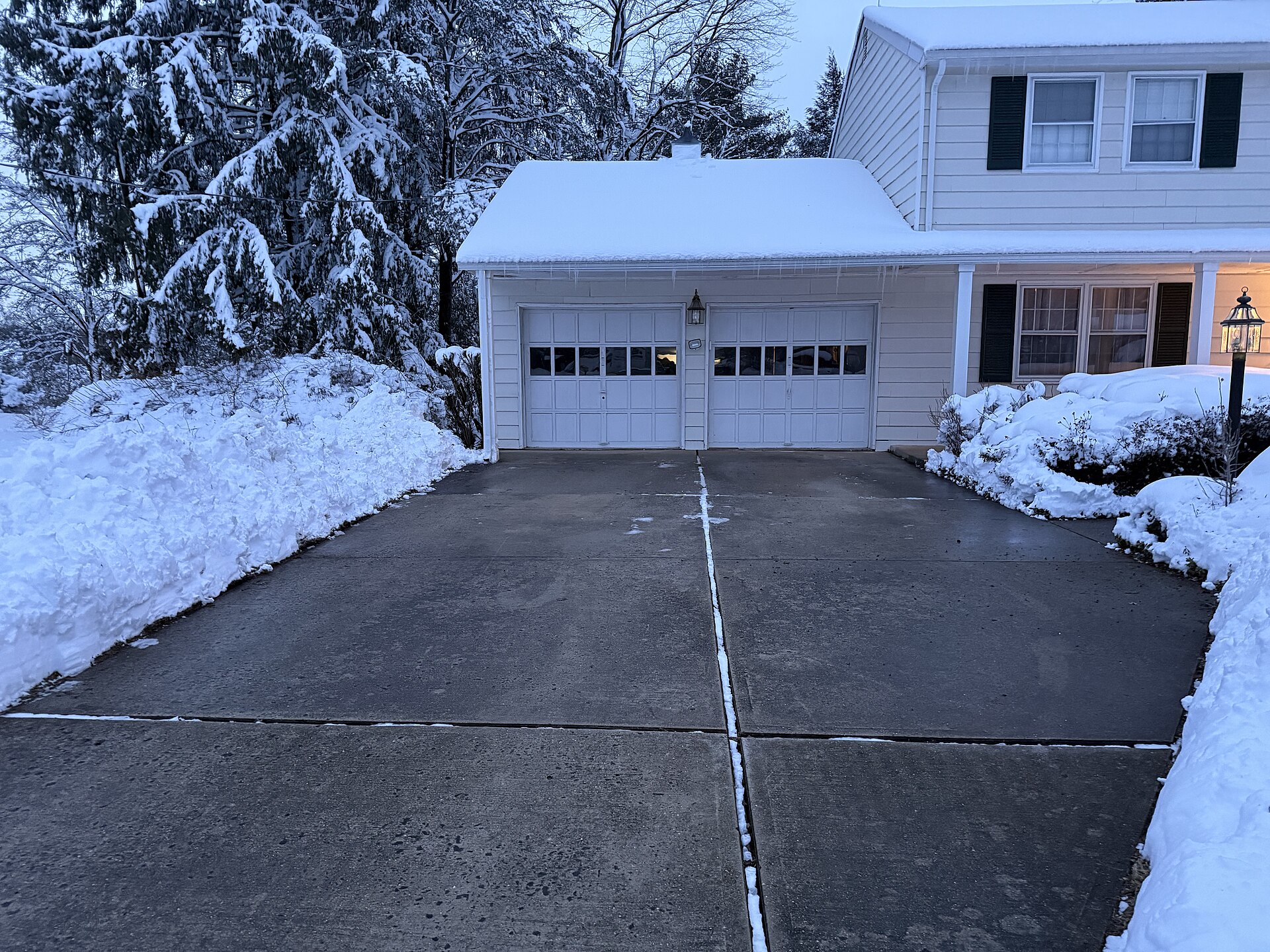 Freshly shovelled concrete driveway leading to a garage, with snowbanks on both sides after a winter storm