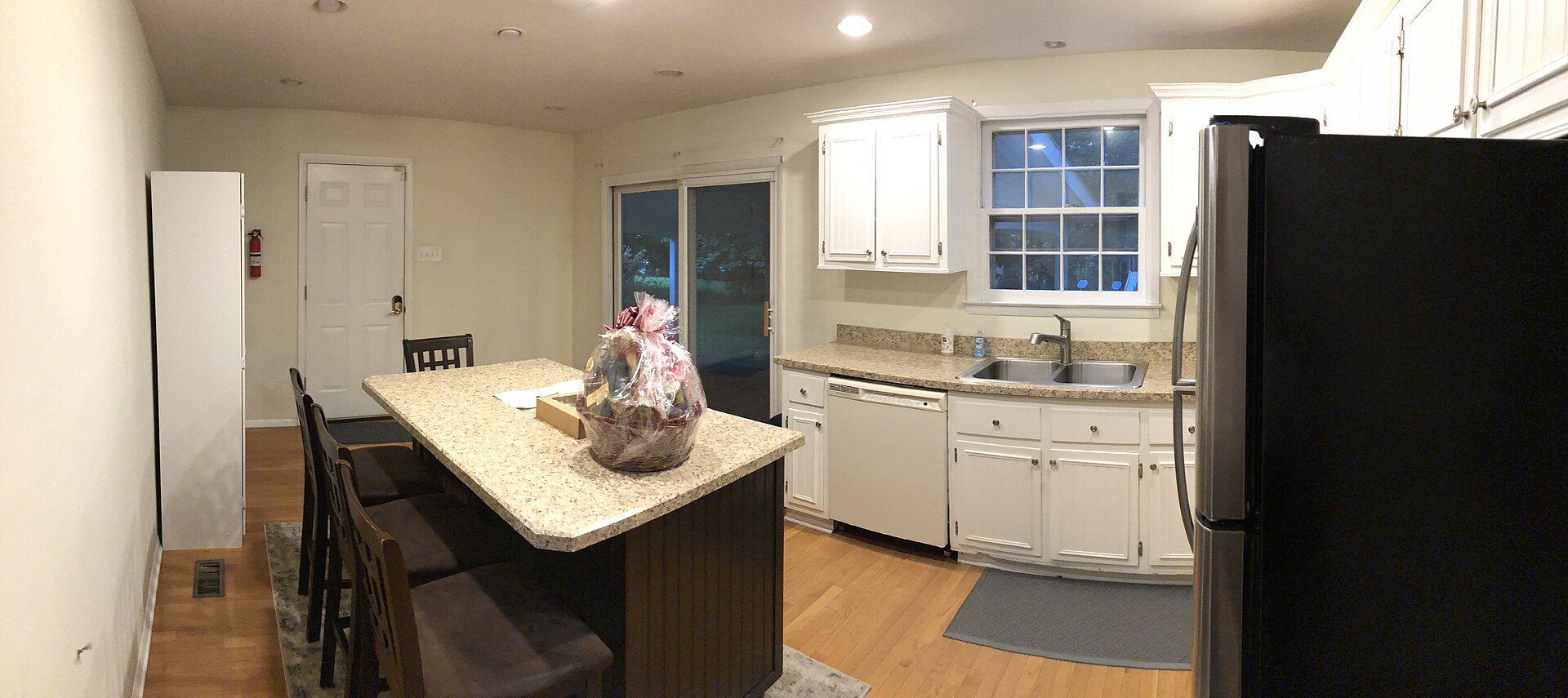 Bright kitchen with white cabinets, granite-topped island with stools, stainless fridge and wood floor