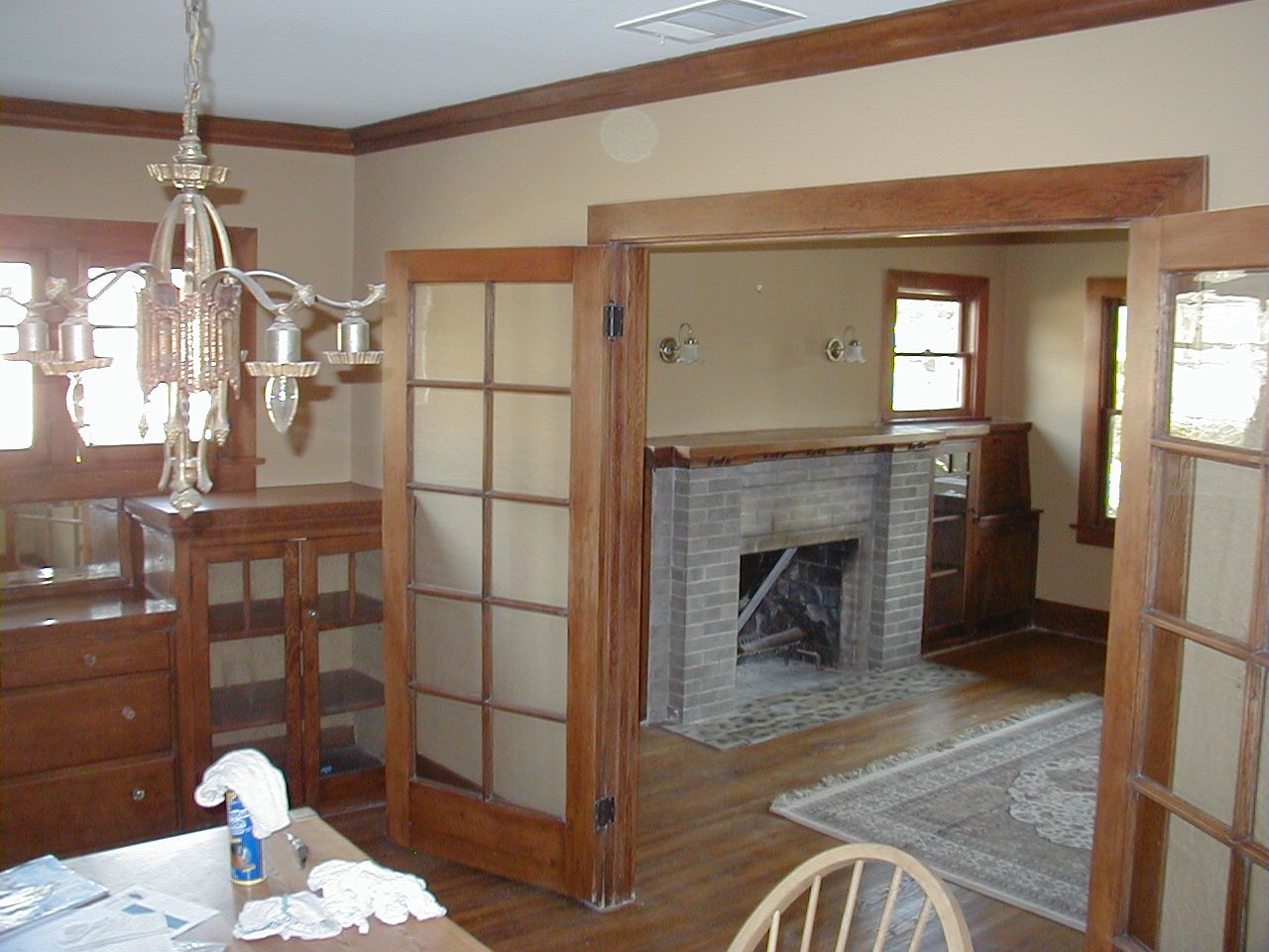 Renovated older home interior looking from a dining room with built-in cabinets into a living room with a brick fireplace