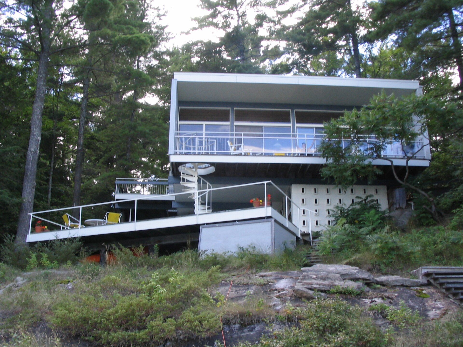 1955 modernist cottage with a wide deck and large windows set on rocks among pine trees in Muskoka