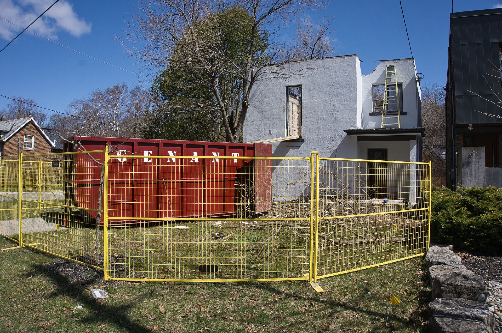 Older house partly demolished behind a yellow safety fence and a red waste bin in the Swansea neighbourhood of Toronto