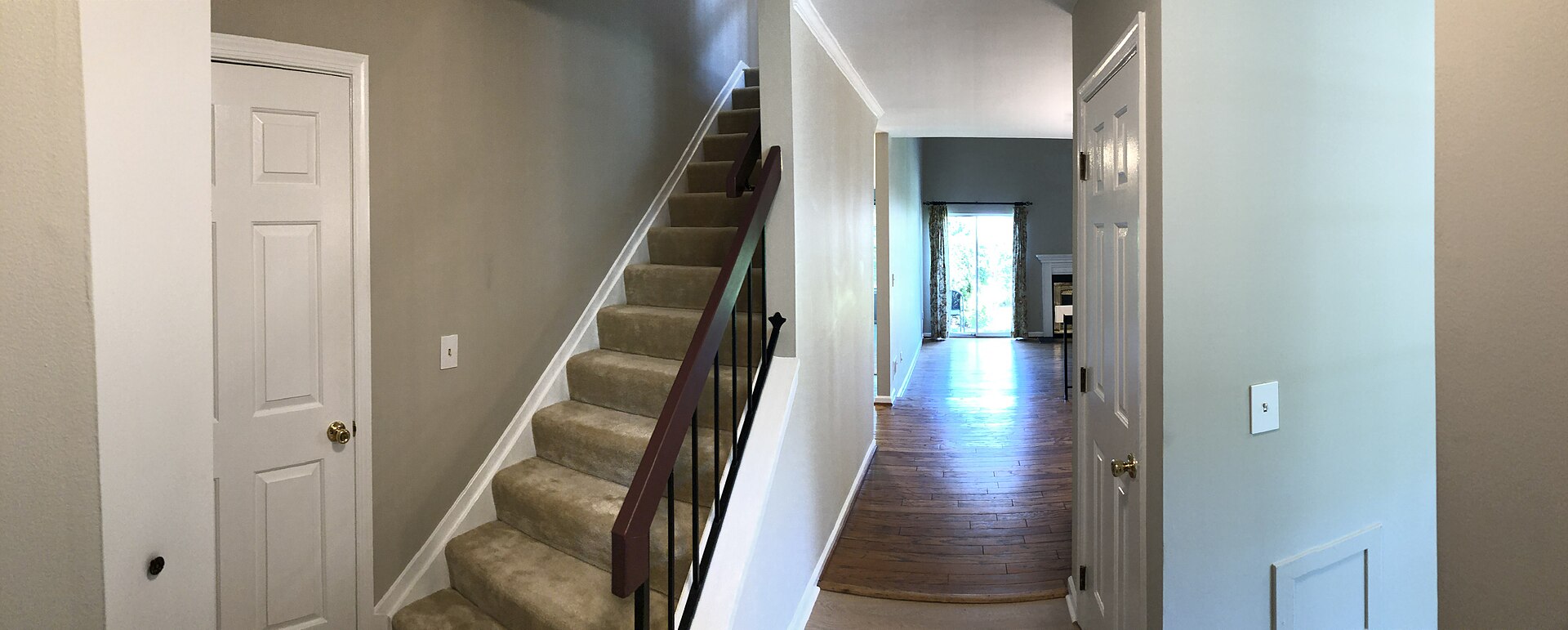 Carpeted staircase rising from a front hallway with wood floor in a two-storey house