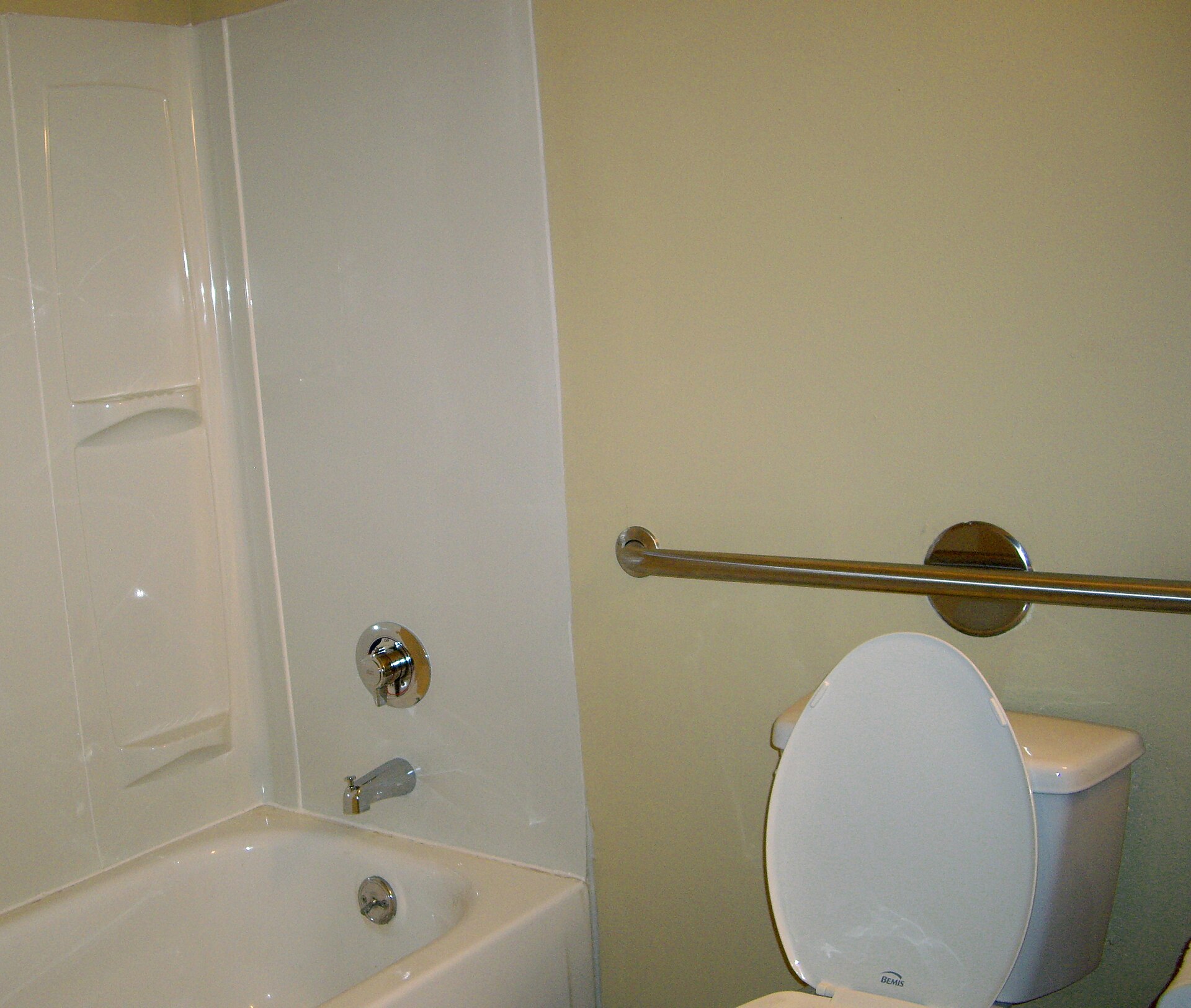 Bathroom with a horizontal stainless grab bar mounted on the wall between a toilet and a bathtub