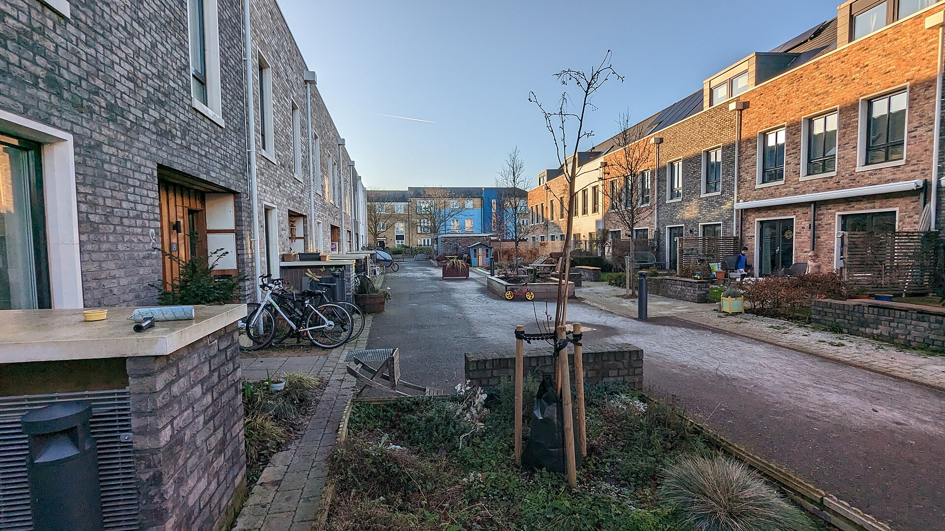 Car-free shared lane between rows of modern brick townhouses with front gardens and parked bicycles