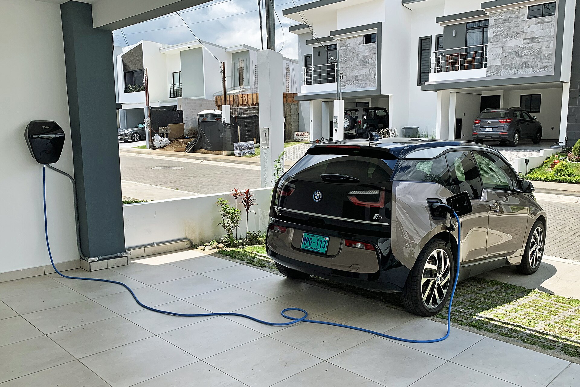 Compact electric car plugged into a wall-mounted Level 2 charger in a covered home carport