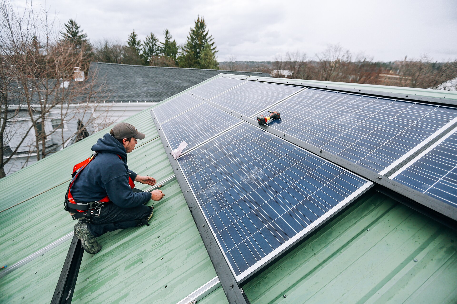 Installer in a safety harness fastening solar panels onto a green metal roof