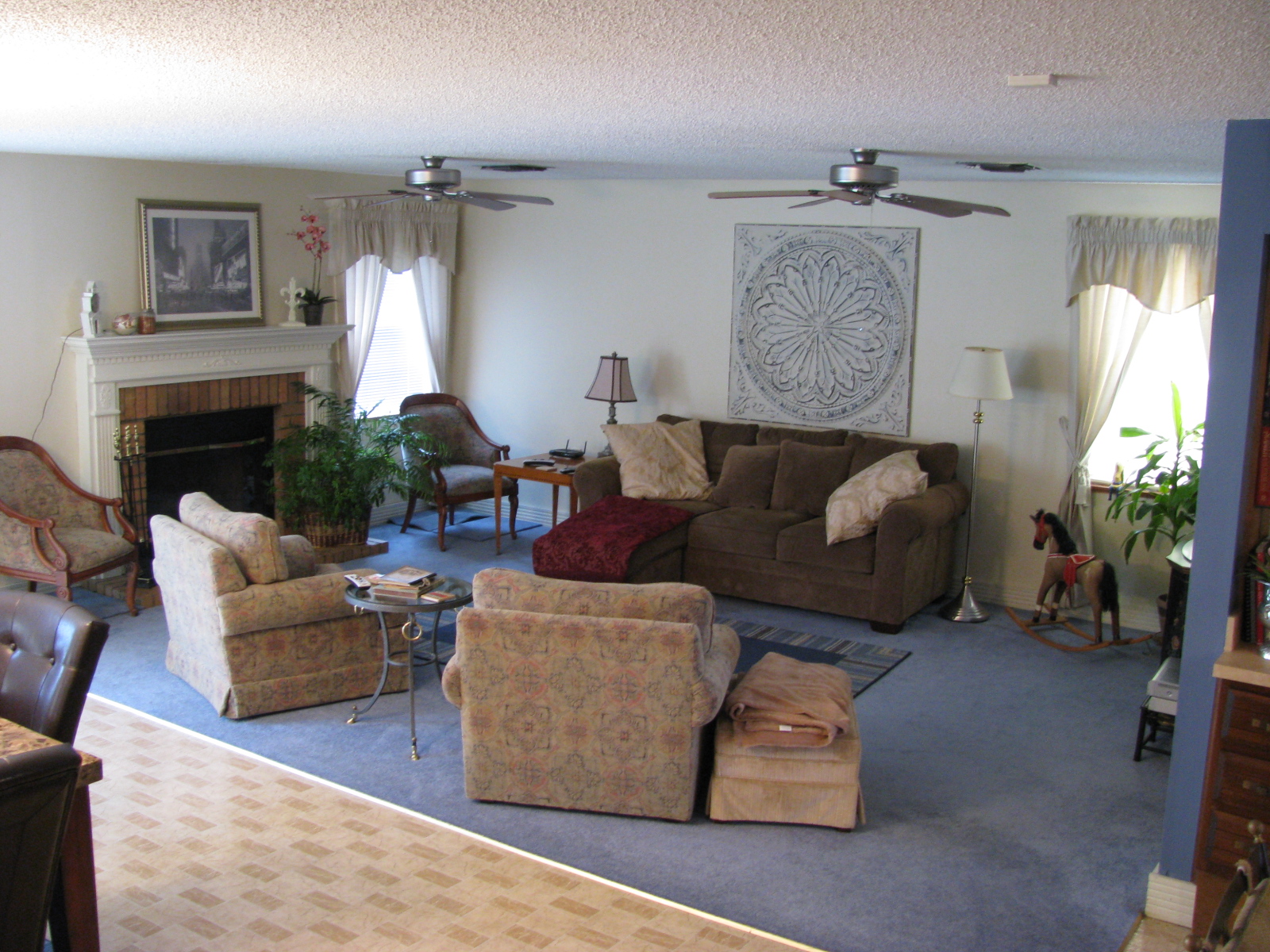 Carpeted living room with sofas, a fireplace and two ceiling fans overhead