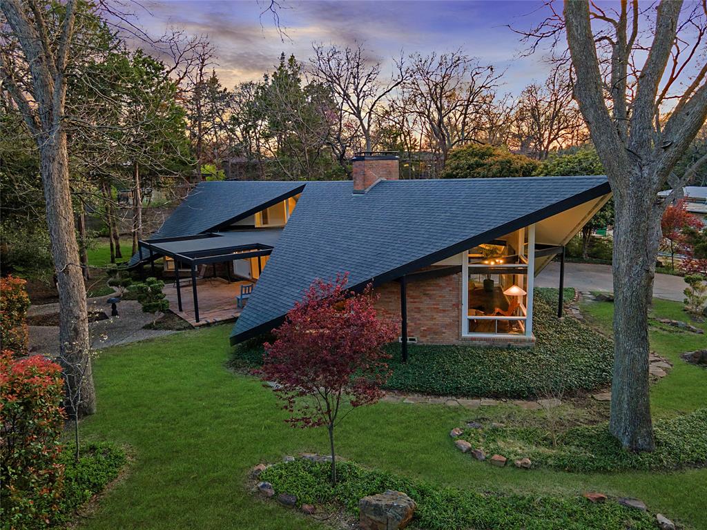 Low mid-century modern one-storey house with a folded, angular roof, brick walls and large glass windows on a treed lot