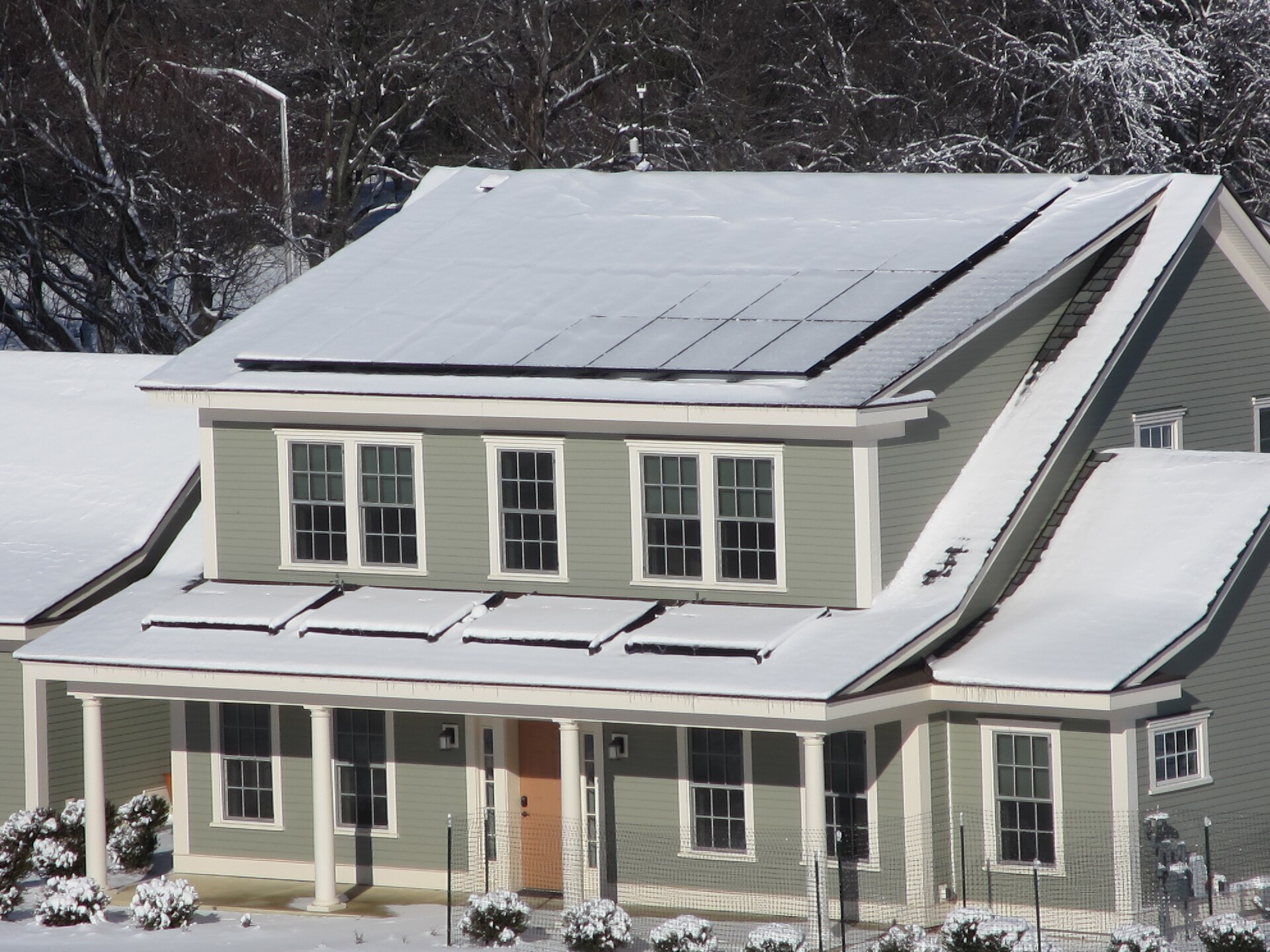 Grey two-storey net-zero test house with roof solar panels and a snowy front yard