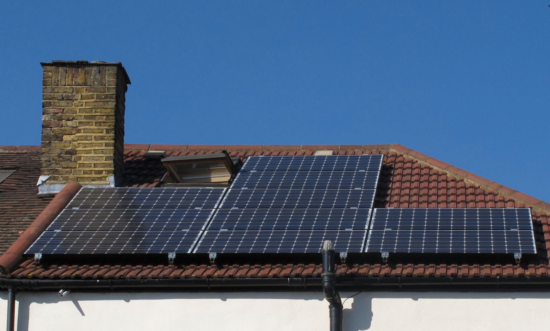 Rows of black solar panels mounted on a pitched tile roof beside a brick chimney