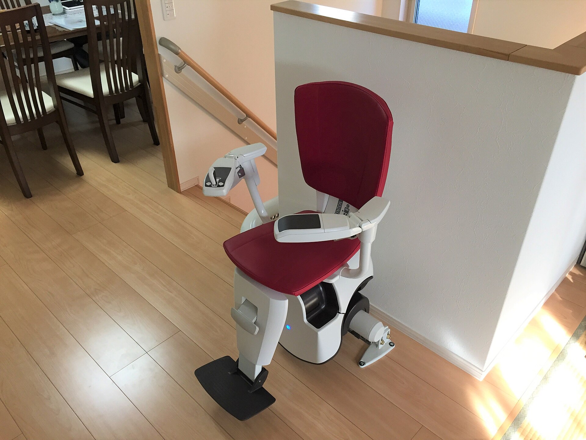 Red-upholstered stair lift chair parked at the top of a curved staircase on a wood floor