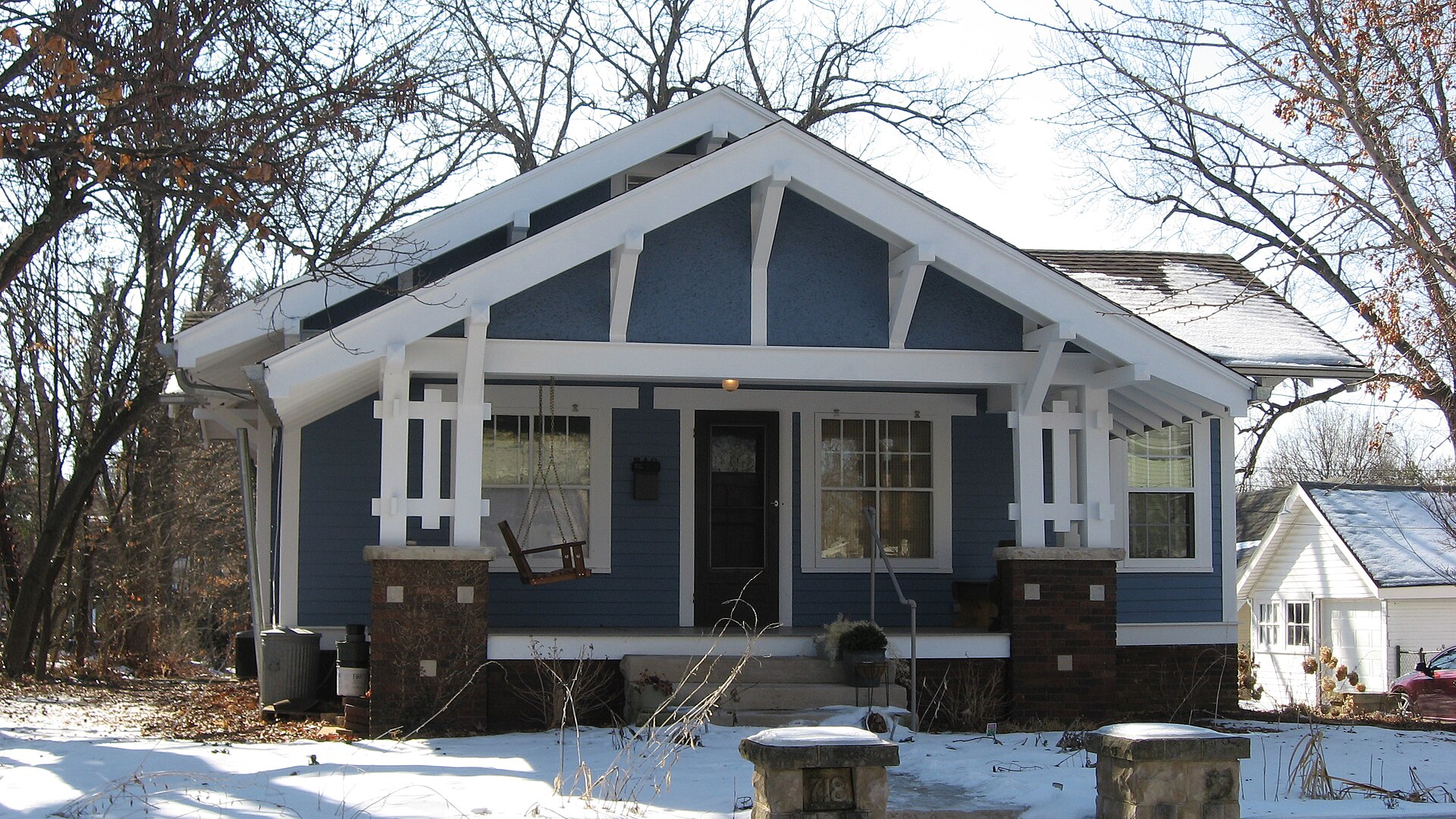 Well-kept Craftsman bungalow with blue-grey siding, crisp white trim, a front gable and brick porch piers in winter