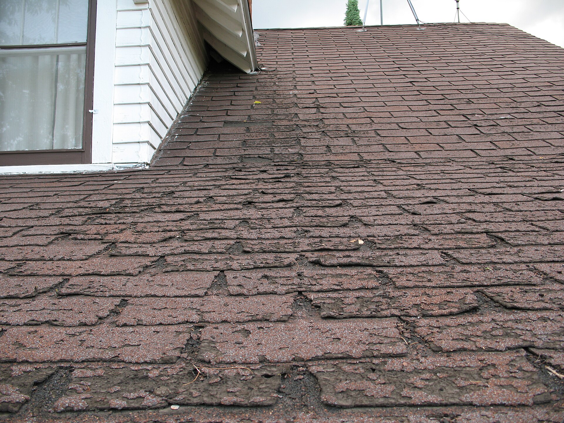 Close-up of weathered asphalt roof shingles worn down along the edge of a roof eave
