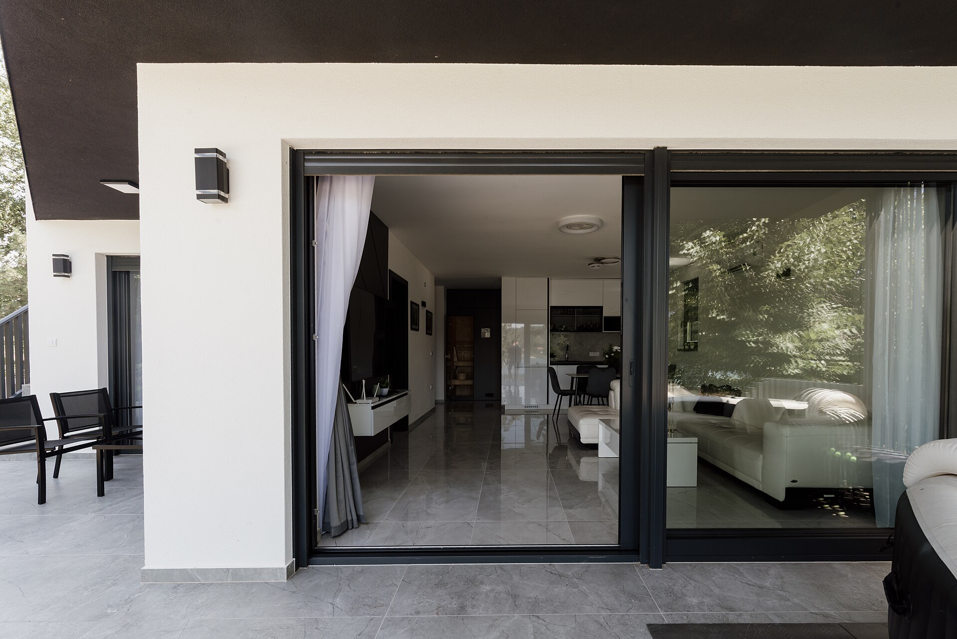 Wide black-framed sliding glass doors opening from a tiled patio into a bright modern living room